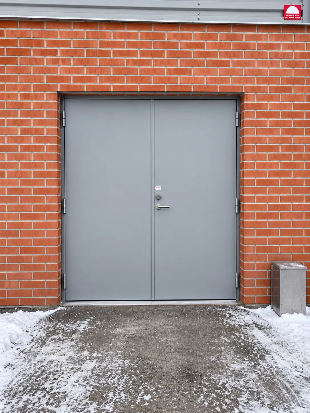 Grå stålpardörr installerad i en utsatt utomhusmiljö